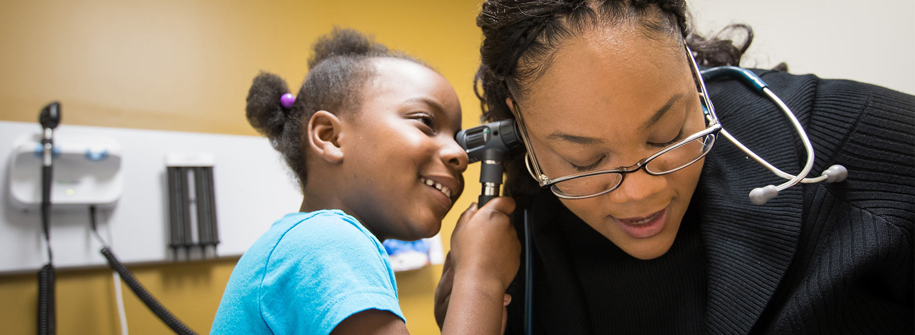 Child looking into provider's ear with scope. Child looking into provider's ear with scope.